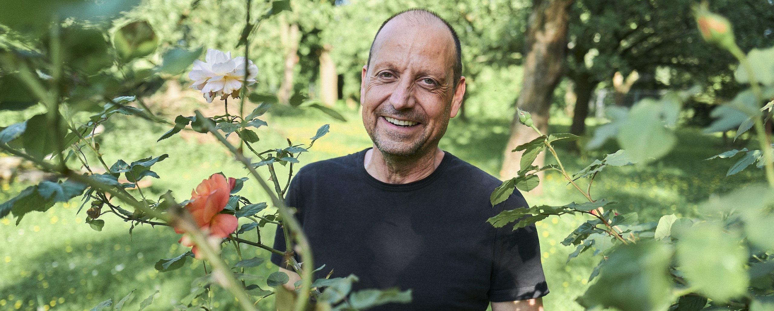 Georg steht hinter einem Rosenstrauch